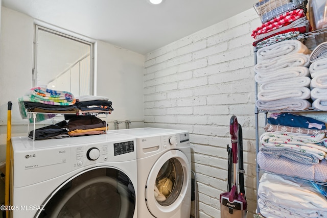 clothes washing area with laundry area, independent washer and dryer, and brick wall