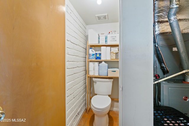 bathroom featuring visible vents, toilet, brick wall, and tile patterned floors