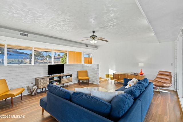 living area with a textured ceiling, ceiling fan, wood finished floors, and visible vents