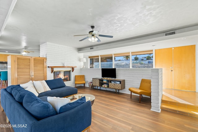 living area with ceiling fan, visible vents, a fireplace, and wood finished floors