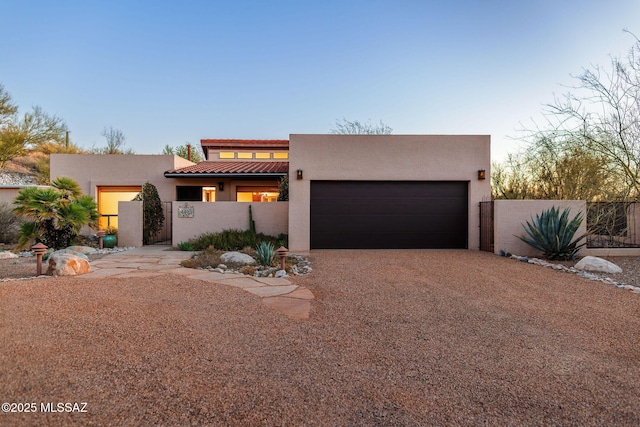 pueblo-style home with driveway, fence, an attached garage, and stucco siding