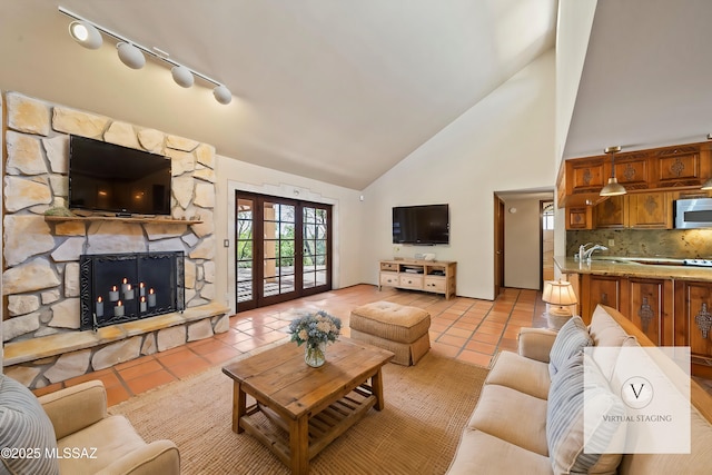 living room with french doors, a fireplace, high vaulted ceiling, track lighting, and light tile patterned flooring