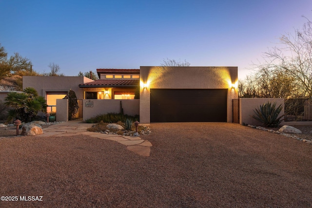 view of front of property featuring a garage, gravel driveway, fence, and stucco siding