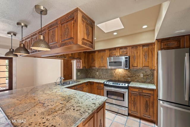 kitchen featuring a skylight, stainless steel appliances, brown cabinetry, a sink, and a peninsula