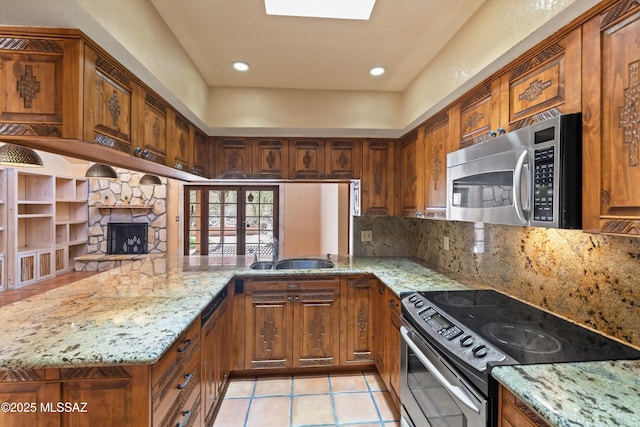 kitchen featuring a peninsula, light stone countertops, stainless steel appliances, and a sink