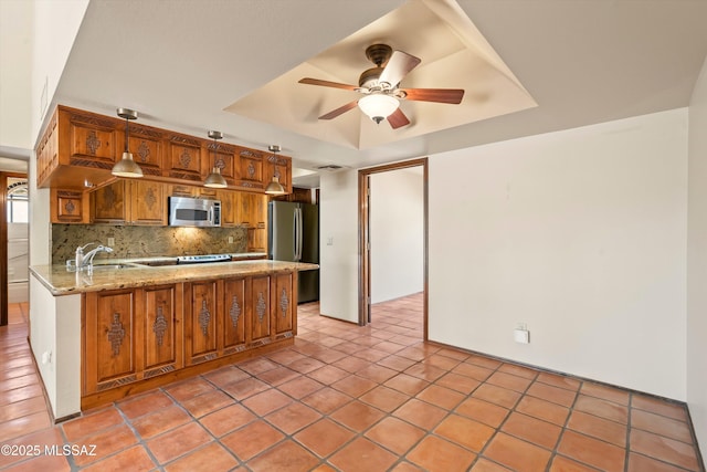 kitchen featuring stainless steel appliances, a raised ceiling, brown cabinetry, a sink, and a peninsula