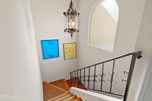 stairway with a chandelier, wood finished floors, and baseboards