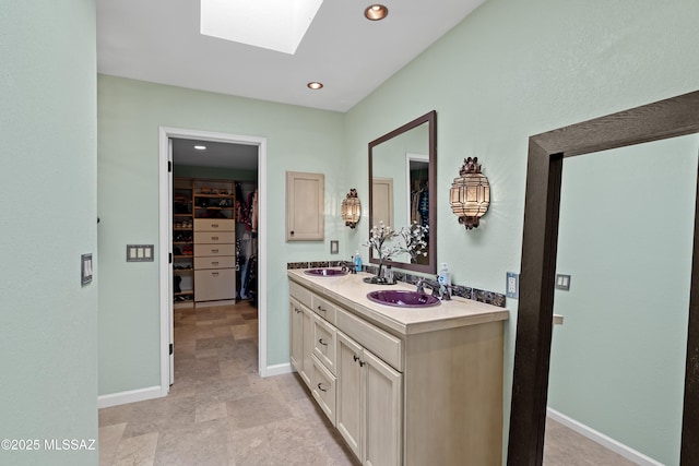 bathroom with a skylight, double vanity, a spacious closet, a sink, and baseboards