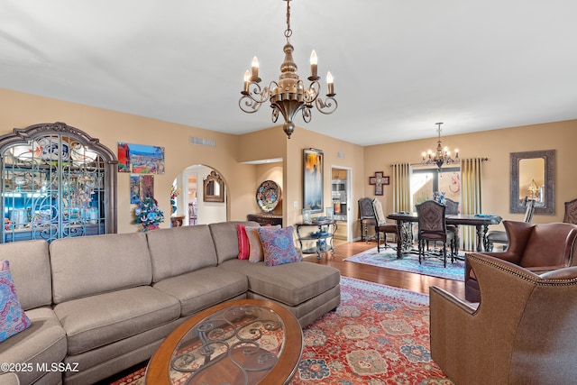 living area with arched walkways, wood finished floors, visible vents, and an inviting chandelier