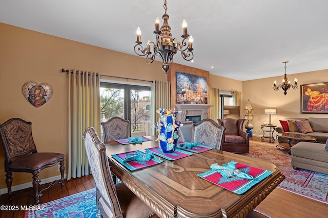 dining area with an inviting chandelier, a fireplace, baseboards, and hardwood / wood-style flooring