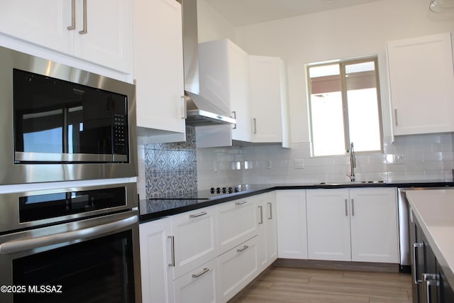 kitchen with decorative backsplash, white cabinets, wall chimney exhaust hood, light wood-type flooring, and a sink