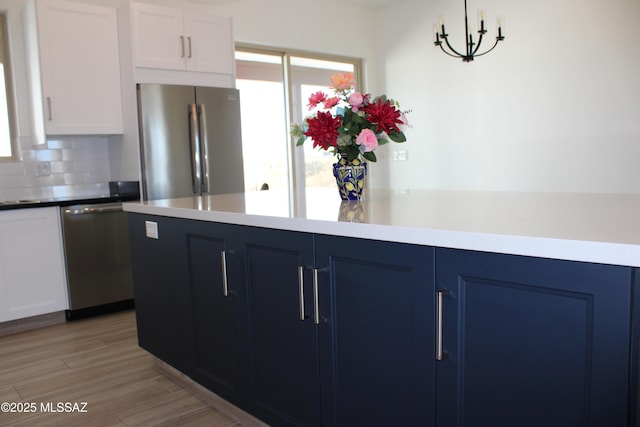 kitchen featuring white cabinets, appliances with stainless steel finishes, blue cabinets, light wood-style floors, and backsplash