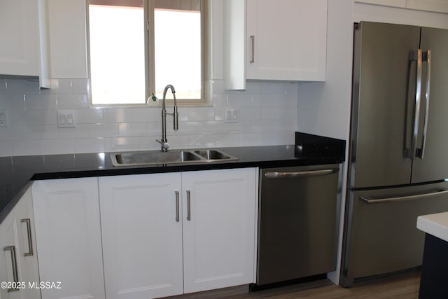 kitchen featuring stainless steel appliances, dark countertops, a sink, and white cabinets