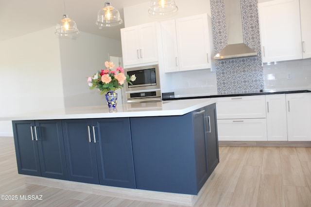 kitchen featuring hanging light fixtures, white cabinetry, stainless steel oven, built in microwave, and wall chimney exhaust hood