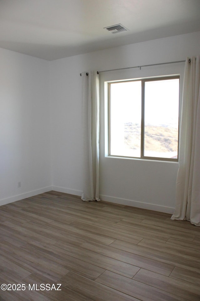 empty room with light wood finished floors, baseboards, and visible vents