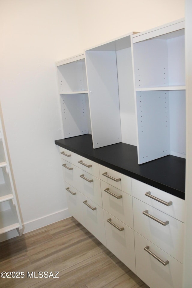 interior space featuring white cabinetry, baseboards, light wood-style floors, open shelves, and dark countertops