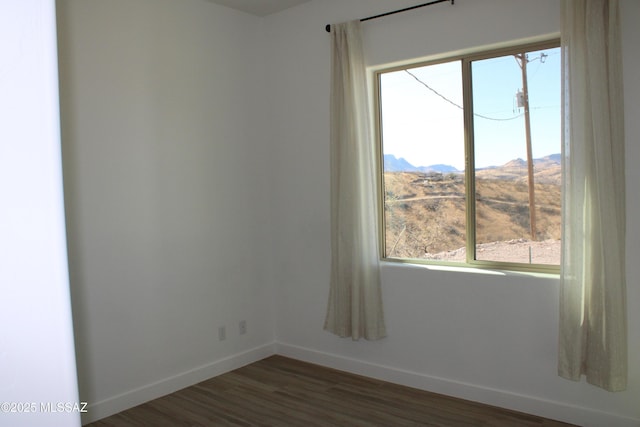 unfurnished room featuring dark wood-style flooring, a mountain view, and baseboards