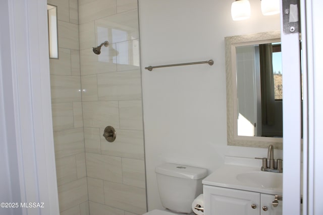 bathroom featuring toilet, tiled shower, and vanity