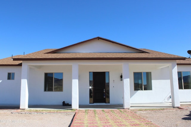 rear view of house featuring roof with shingles, a porch, and stucco siding