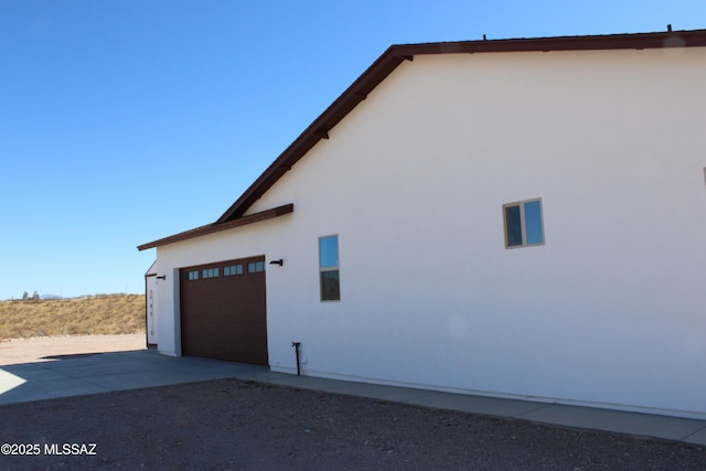 view of side of property featuring driveway, an attached garage, and stucco siding