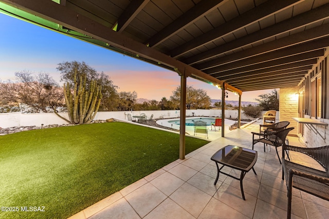 patio terrace at dusk featuring a fenced backyard, a fenced in pool, and a yard