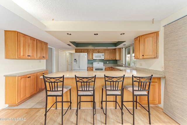 kitchen featuring white appliances, light wood-style flooring, a tray ceiling, and light countertops