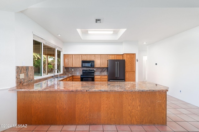 kitchen featuring a peninsula, black appliances, tasteful backsplash, and a sink