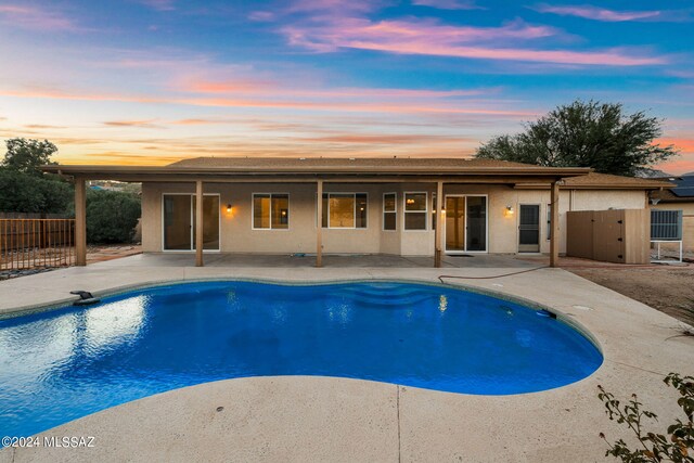 pool at dusk with a patio area, fence, and a fenced in pool