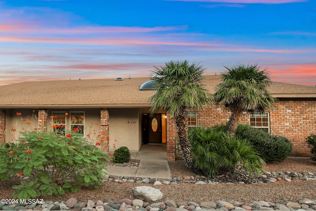 ranch-style house featuring brick siding, roof with shingles, and stucco siding