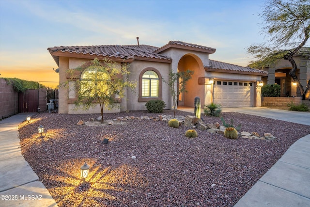 mediterranean / spanish home featuring an attached garage, fence, concrete driveway, a tiled roof, and stucco siding