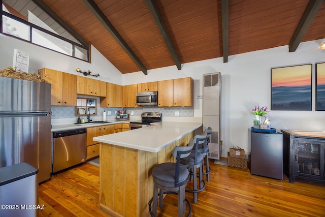 kitchen with tasteful backsplash, appliances with stainless steel finishes, a peninsula, light countertops, and a sink