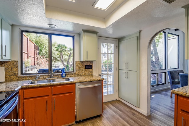 kitchen featuring a textured ceiling, a sink, stainless steel dishwasher, light wood finished floors, and plenty of natural light