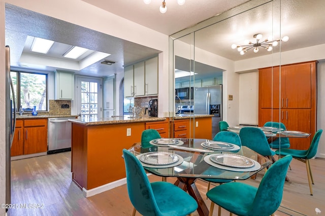 kitchen featuring brown cabinets, light wood finished floors, stainless steel appliances, decorative backsplash, and white cabinetry