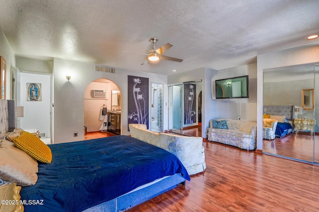 bedroom featuring arched walkways, a textured ceiling, wood finished floors, visible vents, and a wall mounted air conditioner