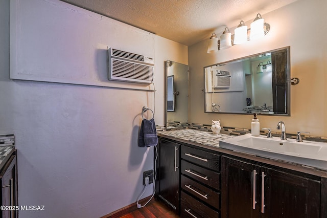 bathroom with baseboards, vanity, wood finished floors, a textured ceiling, and an AC wall unit