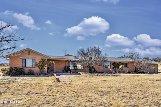 ranch-style house featuring brick siding, a chimney, and a front yard