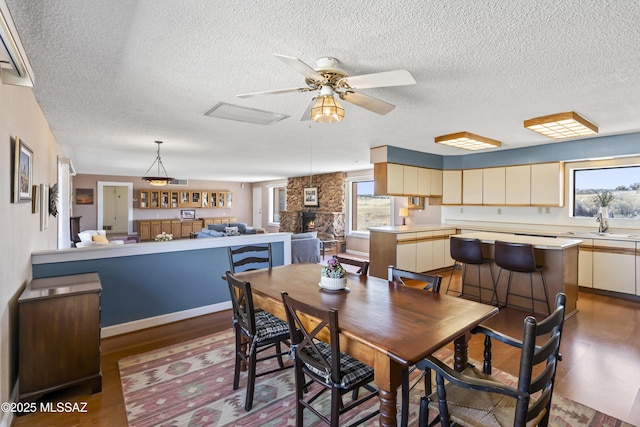 dining space with a textured ceiling, a fireplace, wood finished floors, and a ceiling fan