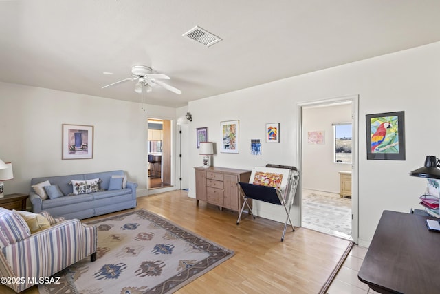 living room featuring light wood-style floors, visible vents, and a ceiling fan