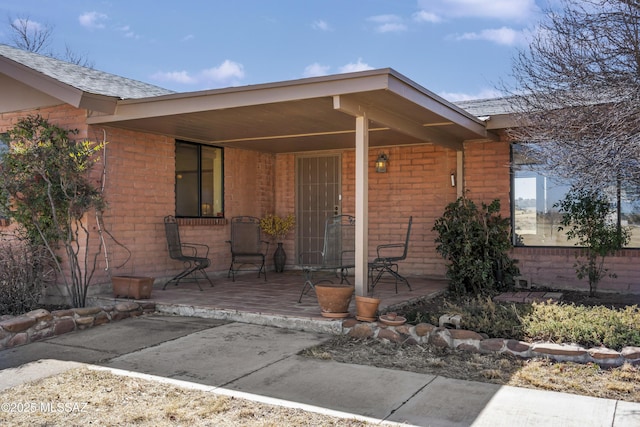 view of exterior entry featuring a patio and brick siding