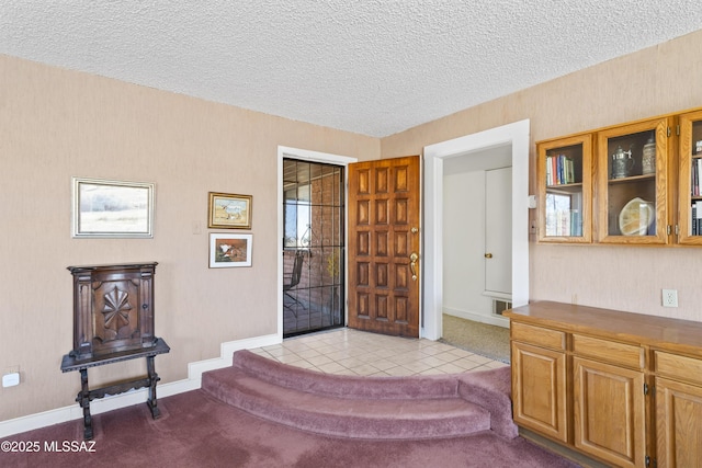 carpeted foyer with a textured ceiling and baseboards