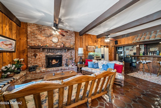 living room featuring visible vents, a ceiling fan, a brick fireplace, wood walls, and beamed ceiling