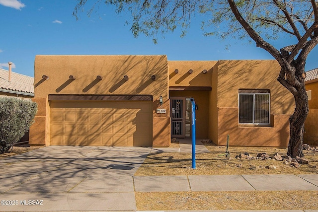 pueblo revival-style home with a garage, driveway, and stucco siding