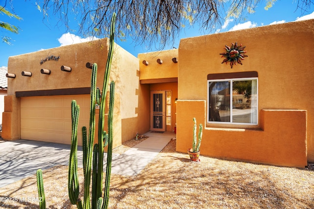 pueblo revival-style home featuring stucco siding, driveway, and an attached garage