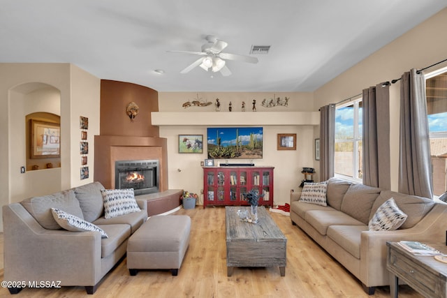 living area featuring light wood-type flooring, visible vents, a ceiling fan, arched walkways, and a fireplace