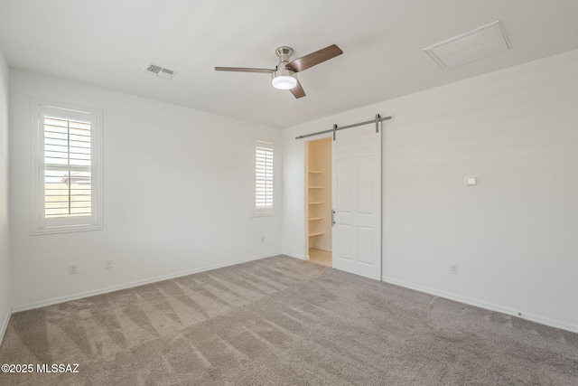 carpeted empty room featuring baseboards, a barn door, visible vents, and a ceiling fan