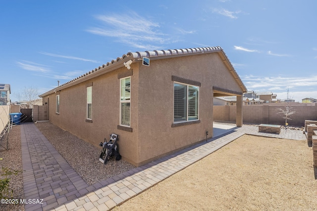 view of property exterior featuring a fenced backyard, a tiled roof, a patio, and stucco siding