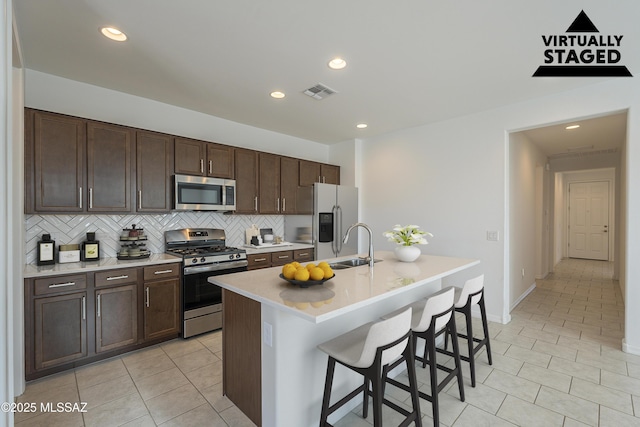 kitchen featuring a breakfast bar, decorative backsplash, appliances with stainless steel finishes, light tile patterned flooring, and dark brown cabinets