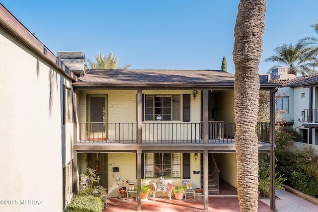 rear view of house featuring a shingled roof and a balcony