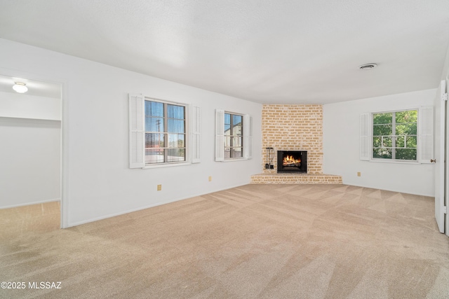 unfurnished living room with a brick fireplace, light colored carpet, visible vents, and a textured ceiling