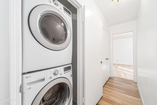 clothes washing area with light wood-type flooring, stacked washing maching and dryer, baseboards, and laundry area